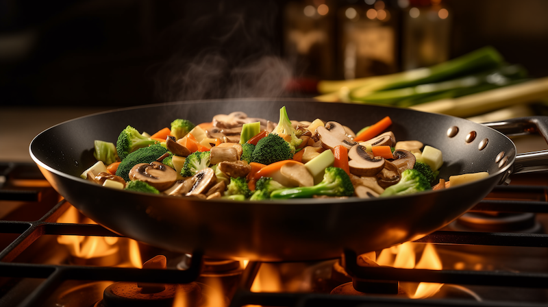 Professional photo of a wok on a stove with chopped onions, broccoli, carrots, spring onions, mushrooms, and zucchini for stir-fry